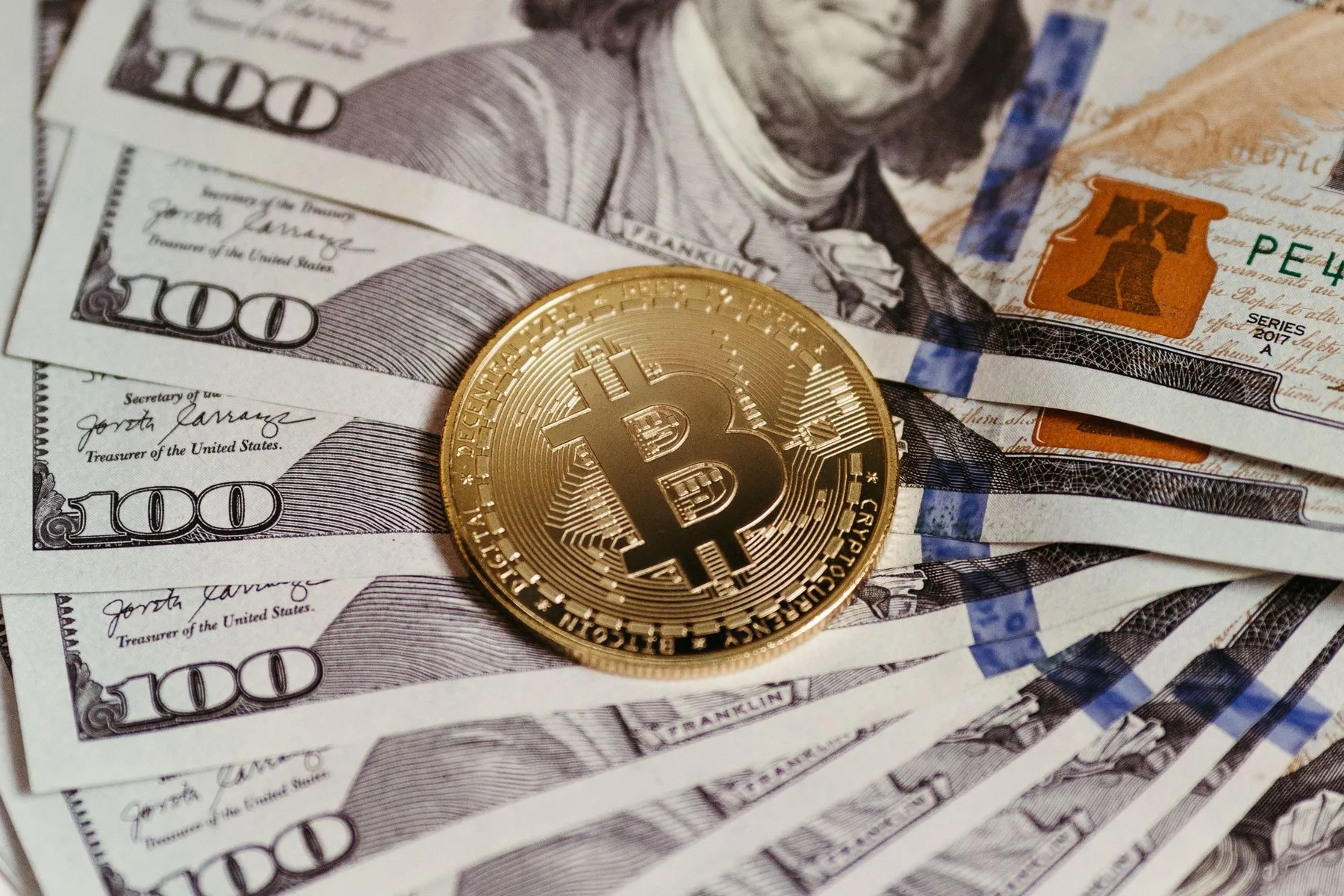 Gold Bitcoin coin lying on a fan of 100 US dollar bills