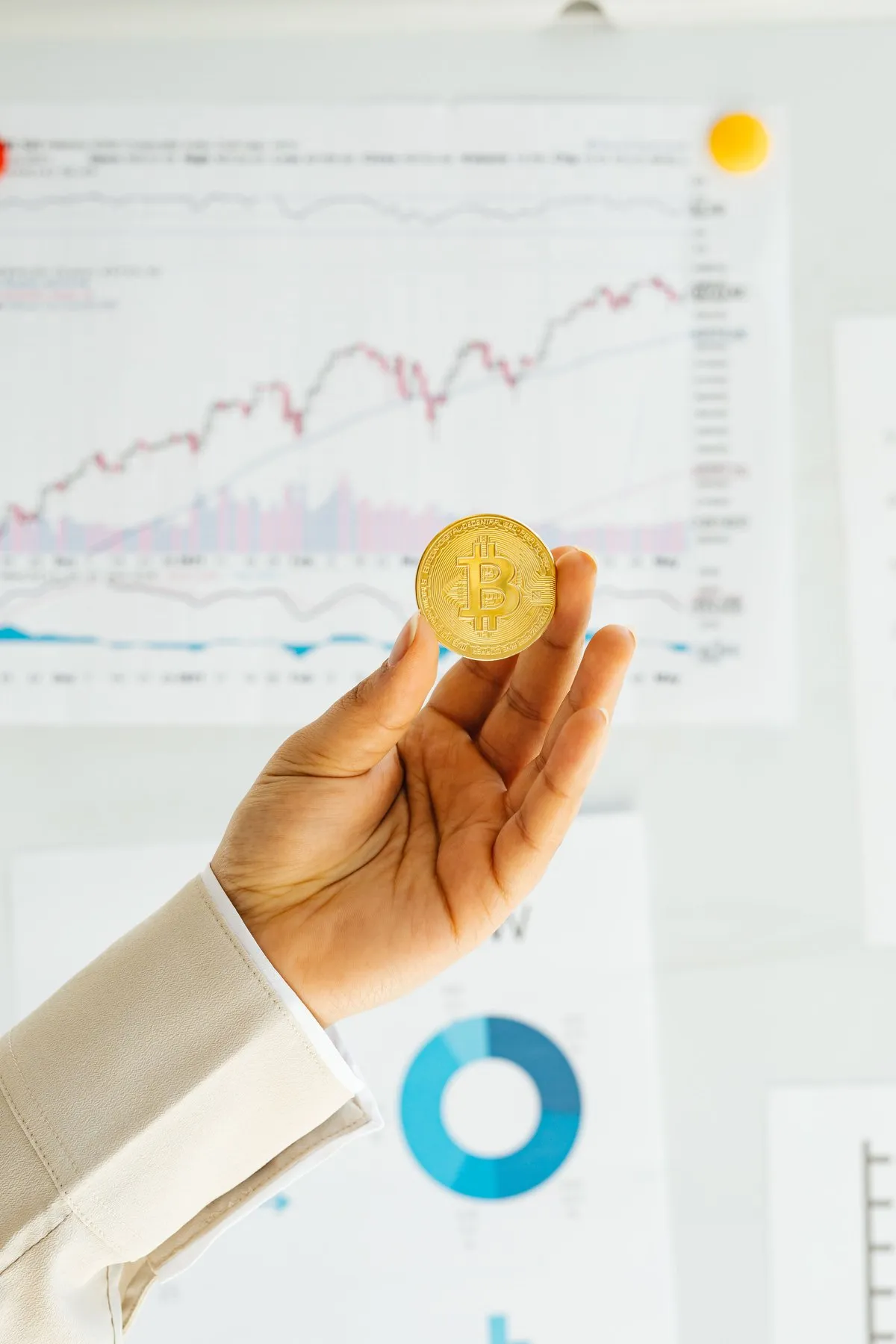 Hand holding a Bitcoin coin over printed analytics charts and a donut graph