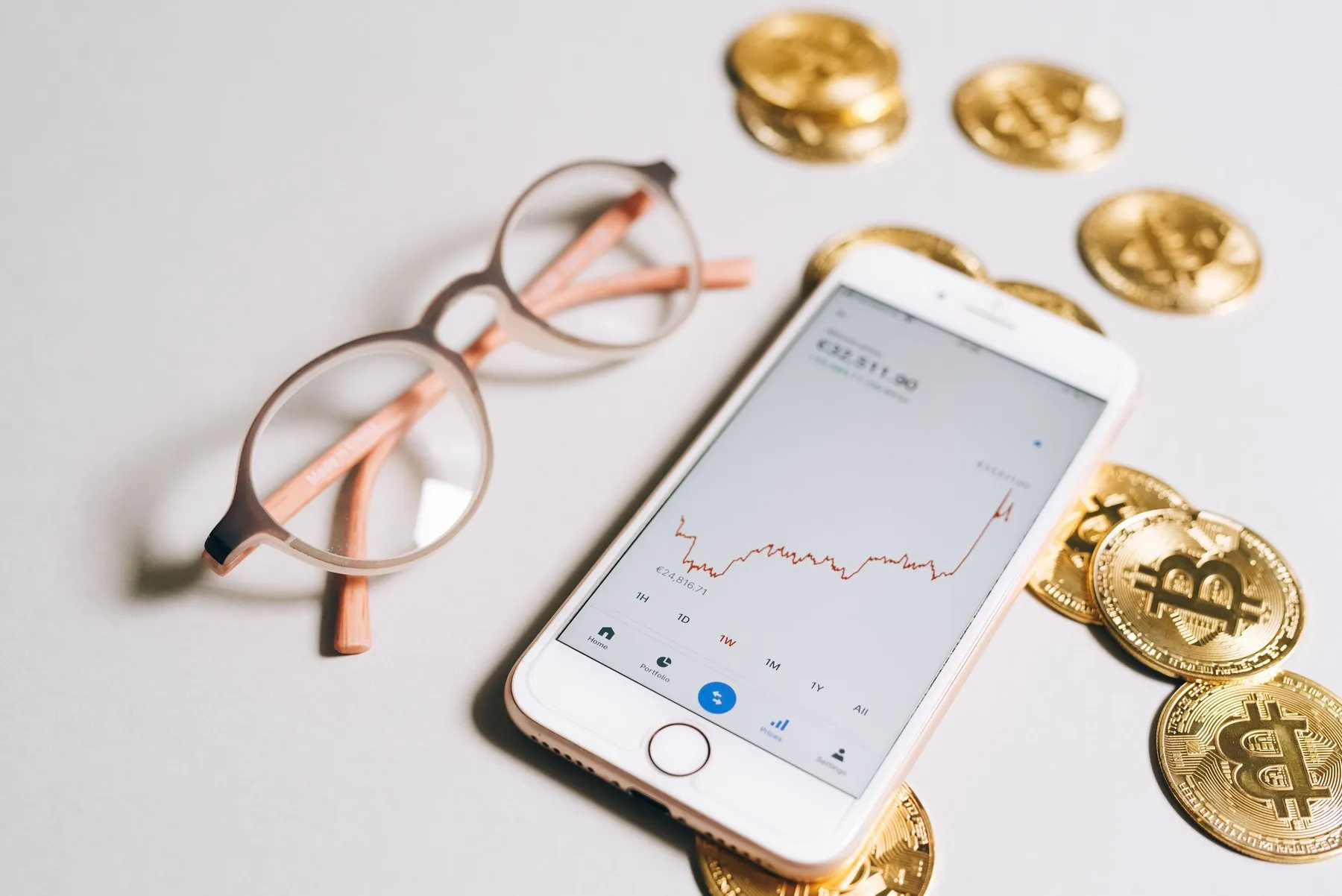 Smartphone with a portfolio app surrounded by gold Bitcoin coins and glasses