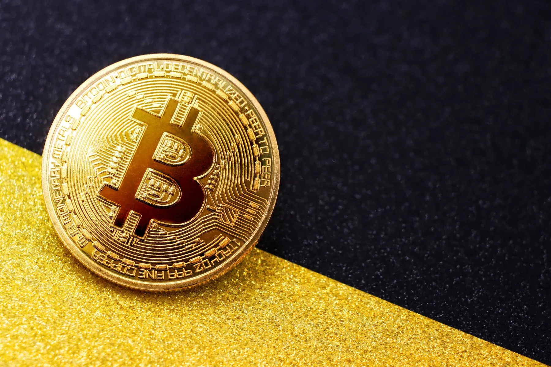 Close-up of a golden Bitcoin coin on a black and gold background