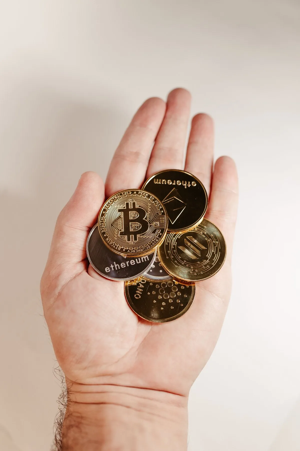 Hand holding a stack of Bitcoin and Ethereum coins against a white background