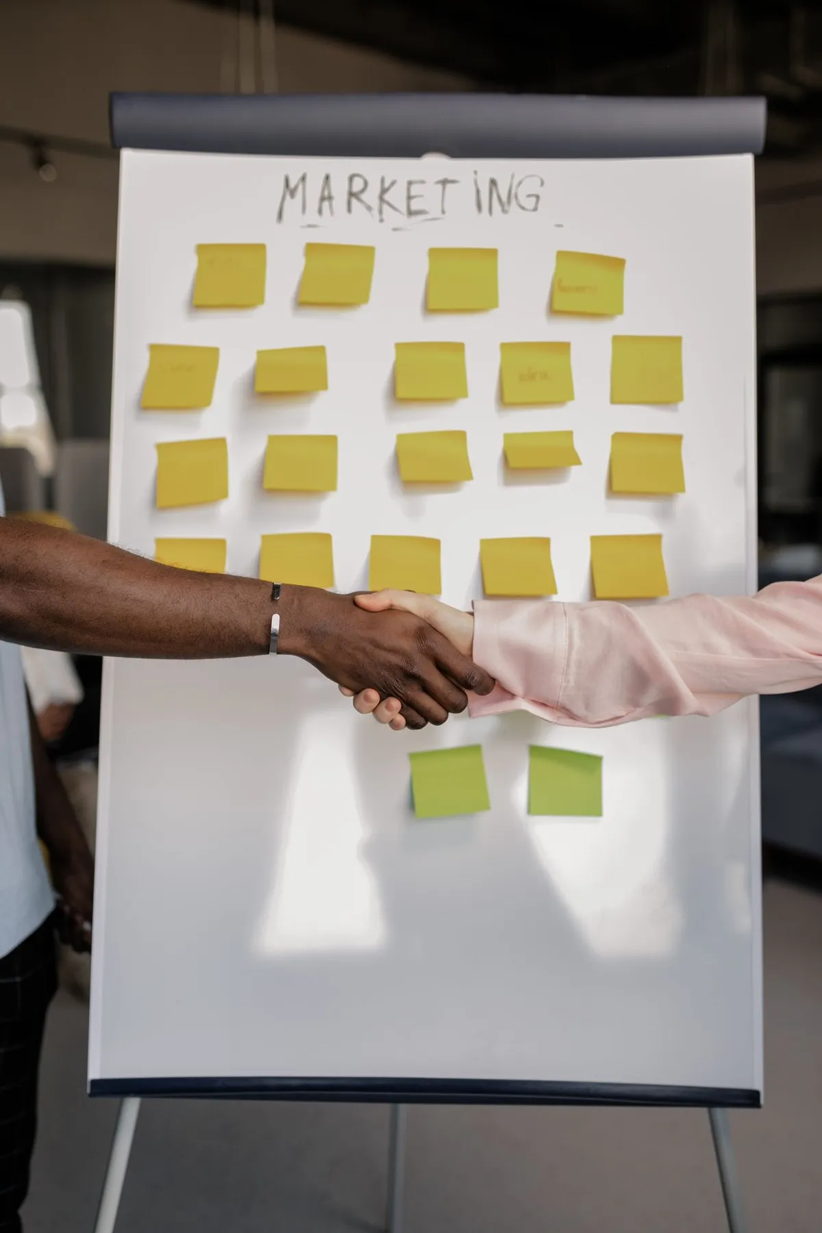 Handshake in front of a flip chart titled Marketing covered with sticky notes