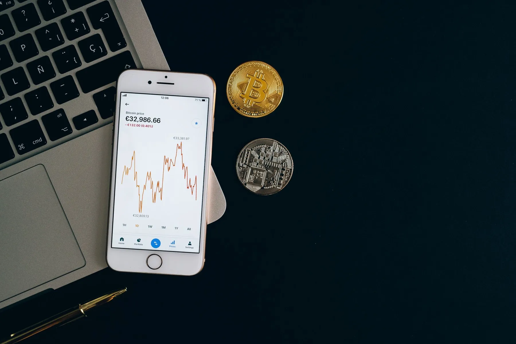 Smartphone with a crypto price chart next to a laptop keyboard and two coins