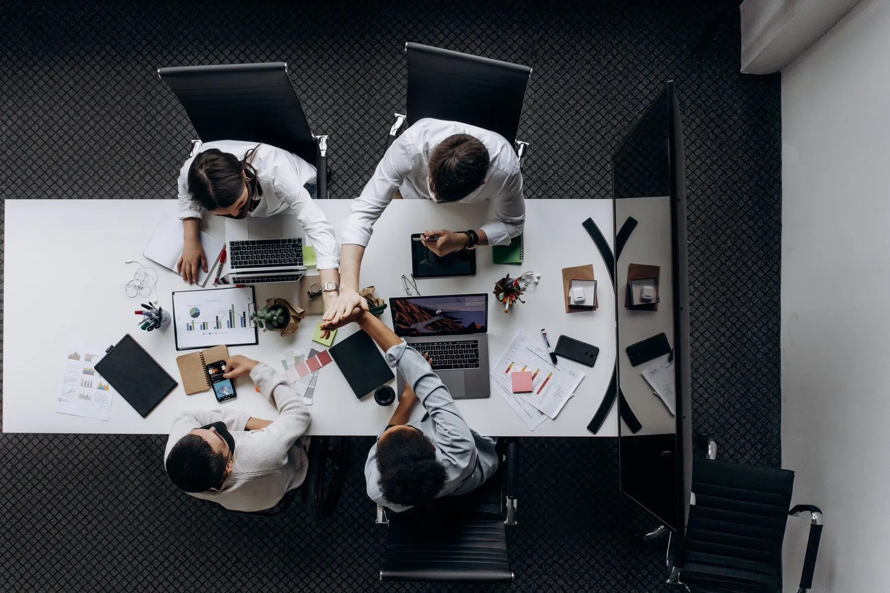 Top view of a team meeting around a white desk with laptops and reports