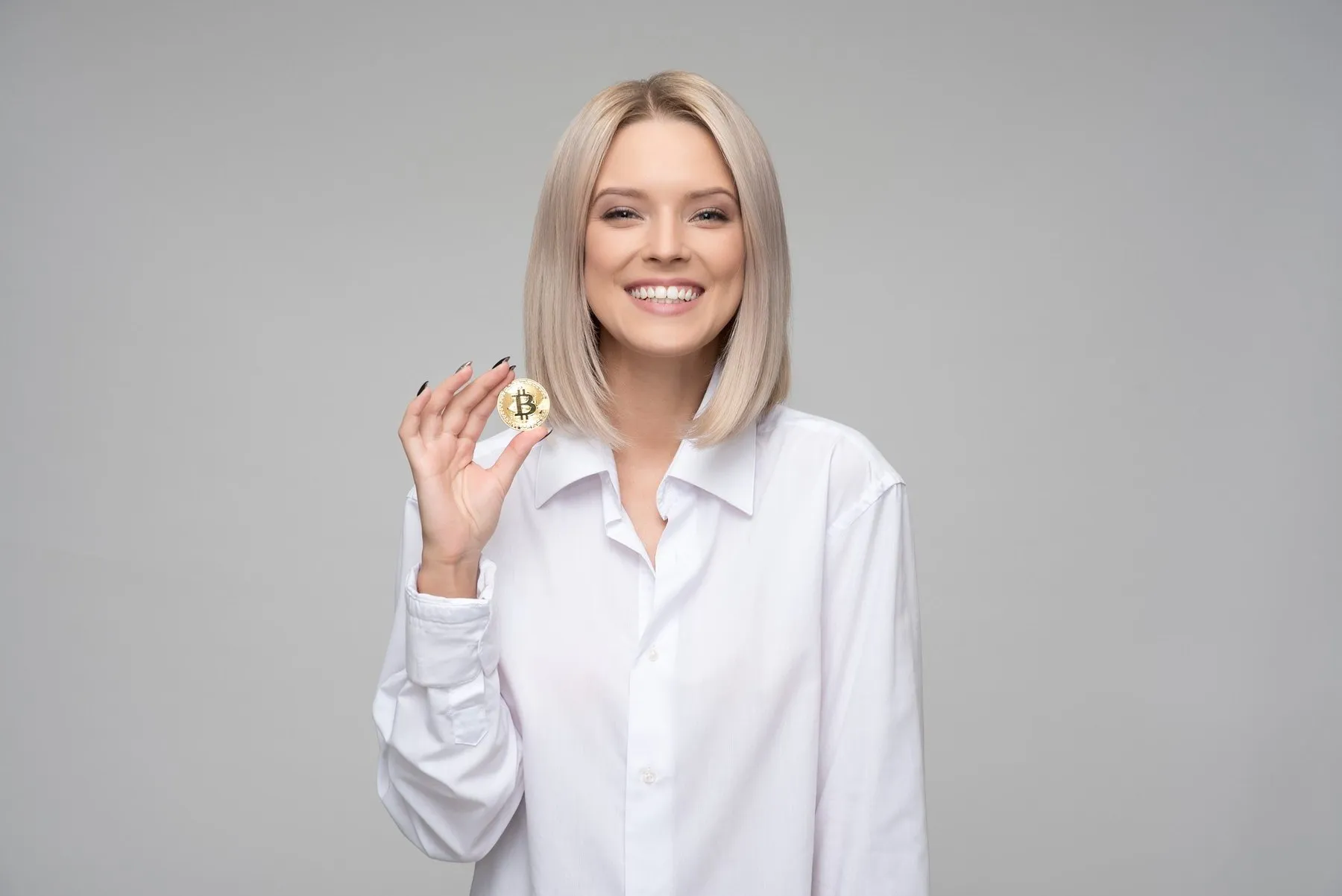 Smiling woman holding a gold Bitcoin coin between her fingers